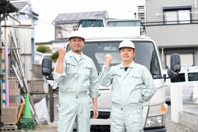 トラックの前でガッツポーズをする作業服を着たミドルとシニアの男性たち